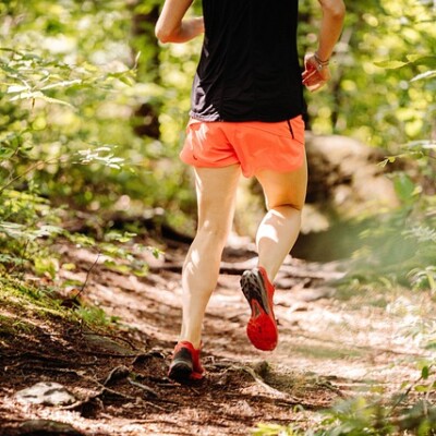 Un coureur en short rose sur un sentier forestier, entouré de verdure.