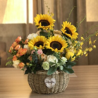 Bouquet de fleurs colorées avec des tournesols, dans un panier en osier sur une table.