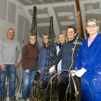 Groupe de bénévoles posant avec des structures de décoration dans un atelier à Feuguerolles-Bully.